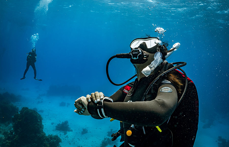 Une plongeuse sous-marine vérifiant son équipement pendant une plongée, avec un autre plongeur en arrière-plan.